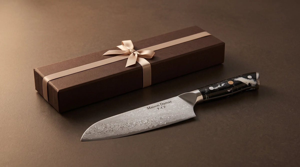Santoku Nagoya Maison Damas et cadeau au ruban champagne dans une ambiance sombre et chaleureuse.
