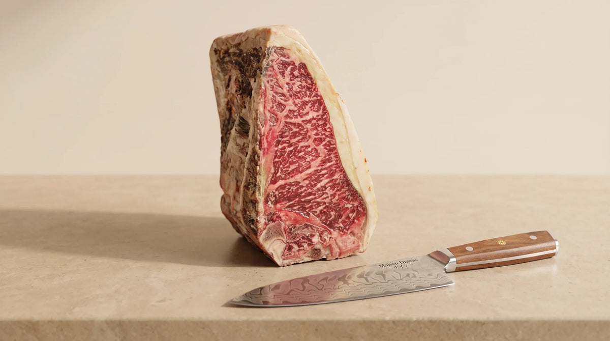 Pièce de bœuf maturée et couteau de chef Miyazaki Maison Damas sur un plan de travail beige.